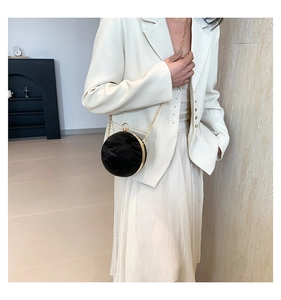 Detail of black round sphere bag with pleated texture and gold chain worn with a white suit