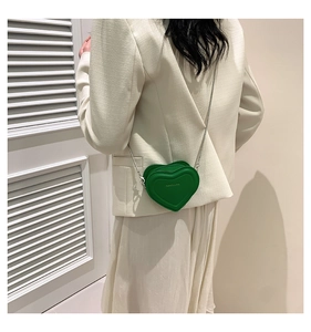 Close-up of a green heart-shaped crossbody bag with a silver chain and embossed text