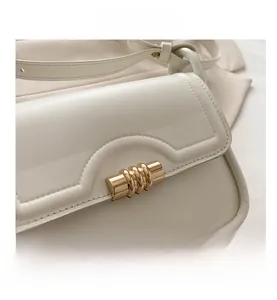 Close-up of cream white leather handbag featuring a textured golden cylindrical metal lock