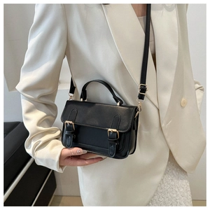 Detail view of a vintage black crossbody bag with gold hardware on a cream blazer