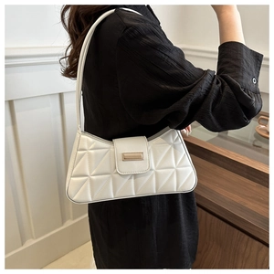 Detail of white quilted baguette bag with gold buckle on shoulder in minimalist interior