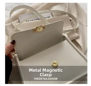 Close-up of golden magnetic hardware closure on a white leather shoulder bag detail