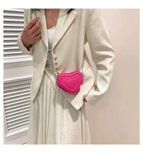 Detail of a bright rose pink heart-shaped crossbody bag with a slim metal chain strap