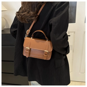 Brown vintage leather crossbody bag worn over a black blazer in a modern home setting