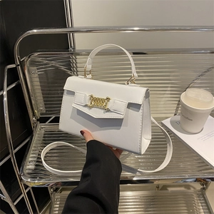 Chic white trapezoid handbag with gold chain lock on a modern silver display shelf