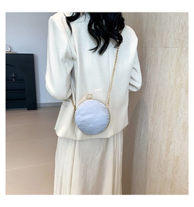 Detail of round light blue crossbody bag with gold metal frame and chain on shoulder