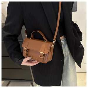 Detail view of brown vintage satchel bag with metal buckles on a black blazer outfit