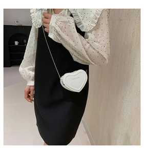Close-up of heart-shaped white crossbody bag with gold lettering and metal chain strap