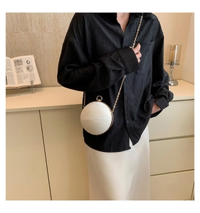 Spherical white pearl-textured crossbody bag with golden chain and round handle worn by model