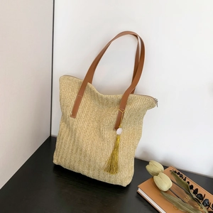 Minimalist straw woven tote bag with brown leather straps and yellow tassel accessory