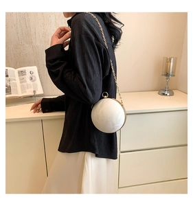 Macro shot of stylish white marble sphere evening bag with gold ring handle and chain strap