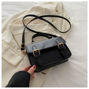 Close-up of minimalist black messenger bag with gold hardware on white textured backdrop