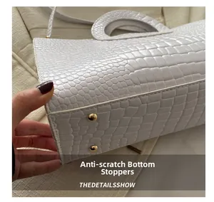 Detail of white crocodile pattern handbag with golden bottom protective studs