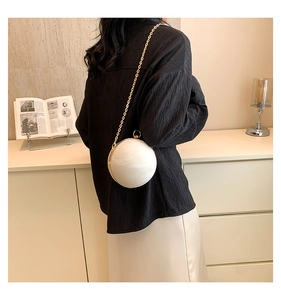 Detail view of the stylish white spherical crossbody bag with gold chain on model