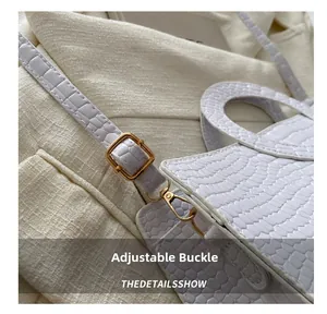 Detail of white crocodile embossed leather bag with adjustable golden metal buckle