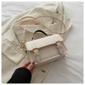 Detail of a creamy white messenger bag with gold buckles and a contrasting black handle