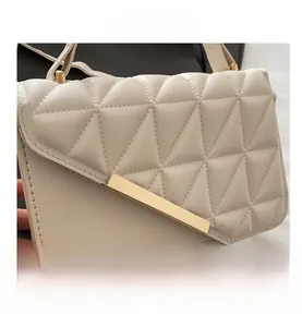 Detail of cream quilted handbag featuring gold metal buckle and geometric stitching