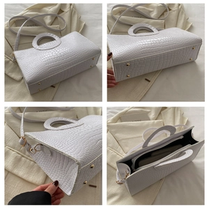 Detail view showing white crocodile embossed tote with metal base studs and shoulder strap