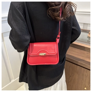Detail of red leather crossbody bag with golden spiral twist lock on a white skirt