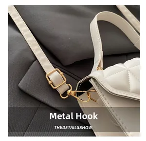 Close-up of polished gold metal hook and buckle on white quilted leather shoulder bag