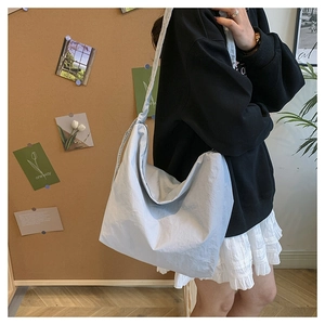 Side view of a light blue nylon drawstring shoulder bag worn in a cozy indoor setting
