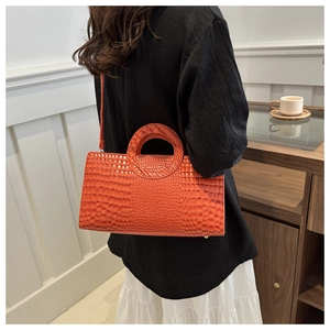 Close-up of bright orange crocodile embossed handbag with a unique cutout ring handle