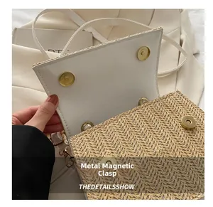 Detail of dual magnetic hardware buckles on a straw woven crossbody bag with white trim