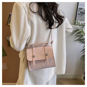 Detail view of pink frosted faux leather crossbody bag with silver buckles on white blazer