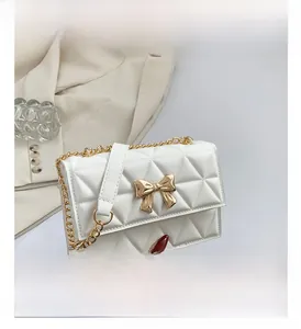 Detail of white quilted crossbody bag with golden metal bow buckle and chain strap
