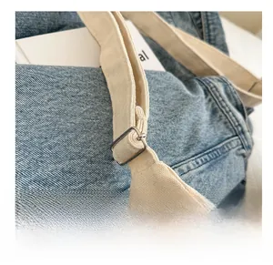 Detail of adjustable silver metal buckle on cream canvas strap with denim background