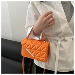 Detail of orange quilted shoulder bag with gold metal trim and triangular stitching