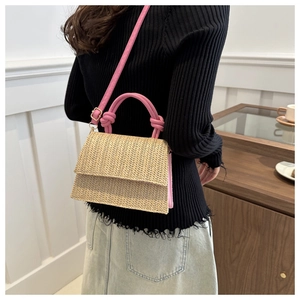 Detail of woven straw crossbody bag with bright pink handles shown in an indoor setting