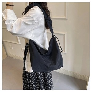 Detail of a black nylon oversized hobo bag showing pleated strap and draped texture on model