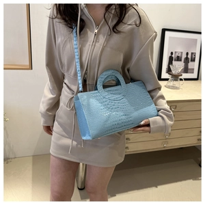 Detail of light blue crocodile pattern handbag with circular handle and thin strap