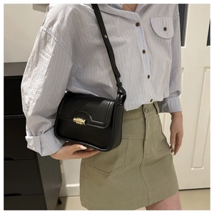 Close-up of stylish black matte flap bag with gold clasp and adjustable strap on model
