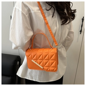 Detail of orange crossbody bag featuring diamond stitching and gold metal bar accent