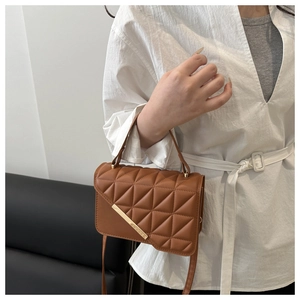 Detail of brown quilted crossbody bag with golden buckle and textured faux leather finish