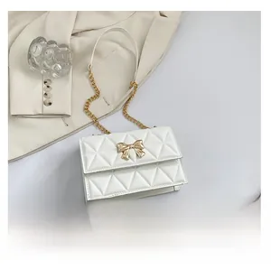 White quilted flap bag detail showing gold bow buckle and smartphone for size reference