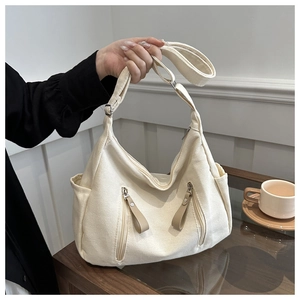 Close-up of off-white canvas hobo bag with zipper pockets and leather pulls on a wooden table