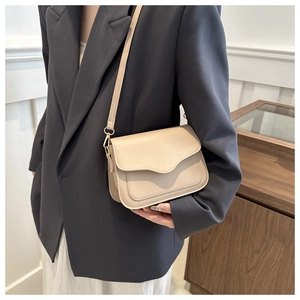 Detail of minimalist beige crossbody bag featuring wavy flap design and slim leather strap