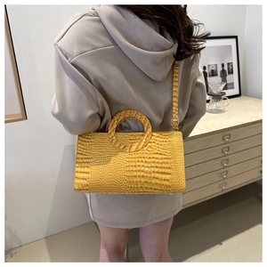 Detail of yellow crocodile pattern handbag showing glossy texture and round handle
