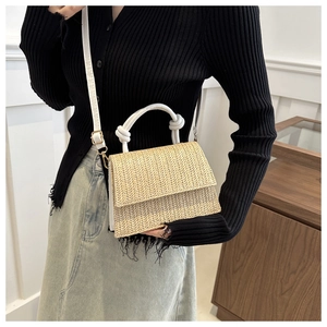Detail of woven straw crossbody bag with white knot handle and golden hardware finish