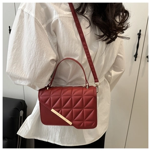 Red quilted handbag with gold metal bar accent shown on shoulder for size scale