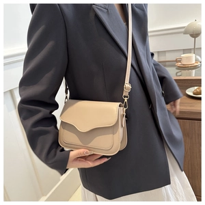 Detail of a beige wave-flap crossbody bag with gold-tone hardware and adjustable strap