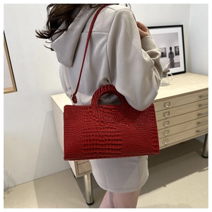 Detail of red crocodile texture handbag with unique circular cutout handle and slim strap