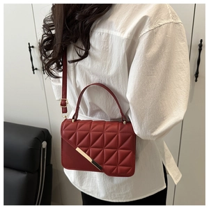 Close-up of geometric quilted red crossbody bag with gold hardware worn by a model