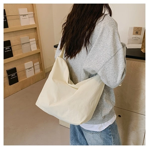 Detail shot of a beige oversized nylon crossbody bag worn by a model in a minimal room