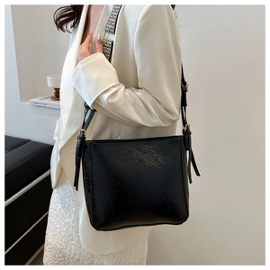 Detail of black glossy bucket bag with geometric woven strap and gold metal hardware