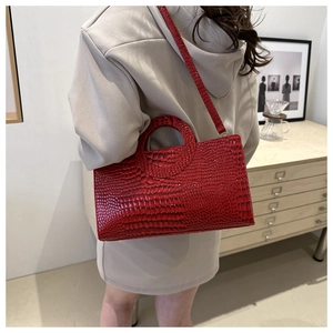 Detail of red crocodile texture handbag with unique circular cutout handle and strap