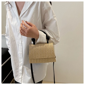 Detail of hand-woven straw crossbody bag with contrast black knotted handle on model